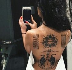 a woman taking a selfie with her cell phone in front of her back tattoo