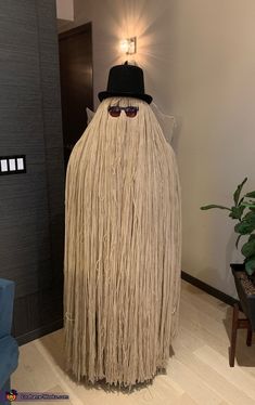 a man in a hat and glasses standing next to a fake mop with long hair