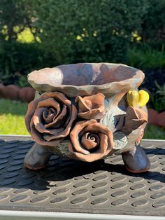 a ceramic flower pot sitting on top of a metal grate in front of some bushes