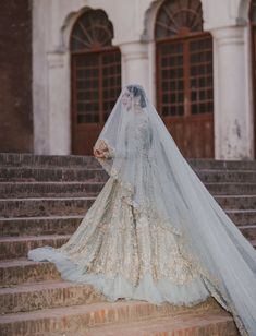 a woman in a wedding dress is standing on some steps with her veil over her head