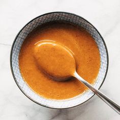 a spoon is in a bowl full of orange colored liquid on a marble table top