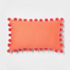 an orange pillow with pom - poms on the bottom and sides, against a white background