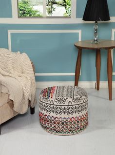 a living room with blue walls and a round foot stool in the corner next to a window