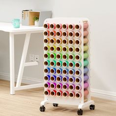 a rack with many rolls of colored thread on it next to a white desk and chair