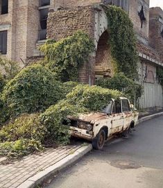 an old truck parked on the side of a road next to a tall brick building