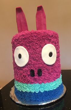 a cake decorated to look like a pink and blue monster with big eyes on a table