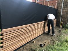 a man standing next to a black fence and wooden slats on the side of a building