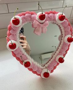 a pink heart shaped mirror with cherries hanging from it's sides and cherry decorations around the edges