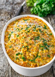 a casserole dish with corn and parsley in it on a wooden table