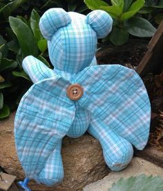 a blue teddy bear laying on top of a rock next to some plants and flowers