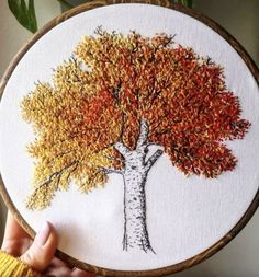 a person holding up a embroidery art piece with an image of a tree on it