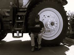 a man sitting on the back of a tractor next to a large tire and holding a laptop