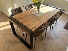 a wooden table with chairs around it and flowers in a vase on the table top