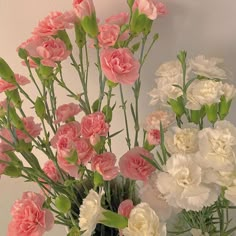 pink and white carnations in a vase on a table next to other flowers