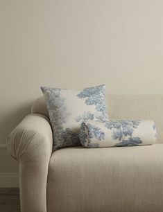 a couch with two pillows on it in front of a white wall and wooden floor