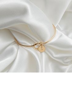 a gold bracelet with a key on it and a white satin fabric in the background