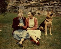 an old photo of two women sitting on the grass with a dog in front of them