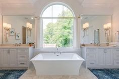 a large white bath tub sitting in a bathroom next to two sinks and a window