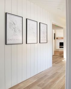 three framed maps hang on the wall next to a hardwood floored hallway with white walls