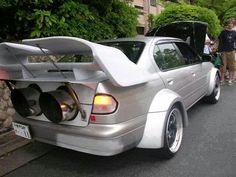 the back end of a silver car with its trunk open and two people standing next to it