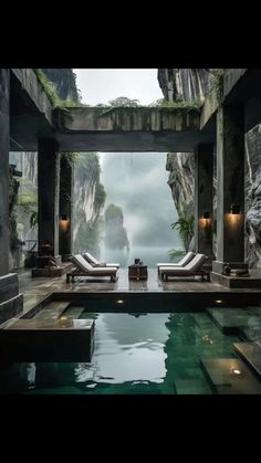 an indoor swimming pool with two chaise lounges next to it and mountains in the background