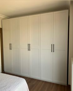 an empty bedroom with white cabinets and wood flooring on the walls, along with a bed