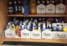 many different types of paint are on display in a cabinet with wooden shelves and cardboard boxes