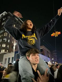 a man sitting on top of another man in the middle of a crowd at night