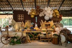 an outdoor party with balloons, decorations and horse drawn carriage for the dessert table in front of it