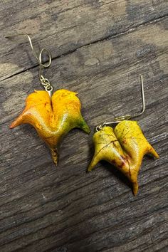 two yellow flowers are hanging from silver earwires on a wooden surface, one is shaped like a leaf