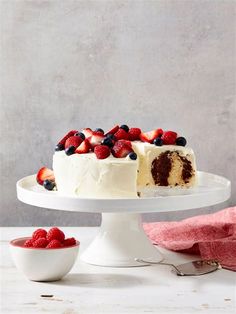 a white cake with berries on top is sitting on a plate next to a bowl of strawberries