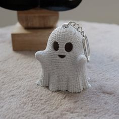 a white knitted keychain shaped like a ghost sitting on top of a bed