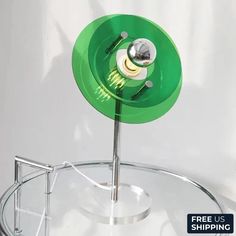 a green object is sitting on top of a metal stand with a free us shipping sign below it