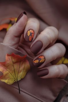 Capture the essence of fall with these chic brown nails, adorned with vibrant orange and yellow leaf designs. Perfect for the fashion-forward, this trendy fall nail design adds a seasonal touch to your look. Whether you're cozying up for the season or attending an autumn event, these stylish nails are the perfect accessory to elevate your fall fashion game! Fall Leaf Design Nails, November Themed Nails, Fall Leaf Nails Autumn Leaves, Oval Nails Halloween, Leaf Nails Fall, Brown And Orange Nails Fall, Autumn Leaf Nails, Fall Leaf Nail Designs, Trendy Autumn Nails