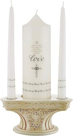 two white candles sitting on top of a stand with the word love written in it