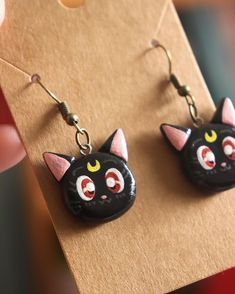 a pair of black cat earrings with red eyes and yellow ears are on a piece of brown paper