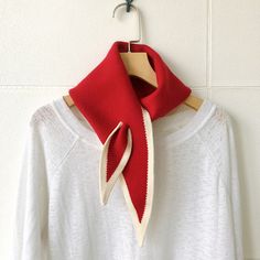 a red and white scarf hanging on a wall next to a wooden hanger with clothes