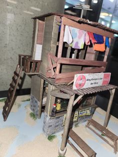 a doll house made out of wood with clothes hanging from the roof and stairs leading up to it