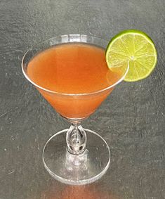 an orange drink in a martini glass with a lime slice on the rim