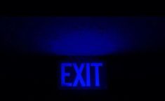 an exit sign lit up in the dark with blue light coming from it's side