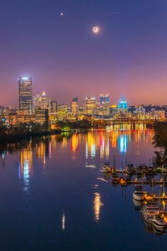 the city lights shine brightly in the distance as boats sit on the water at night