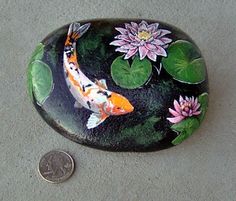 a penny sitting next to a painted rock with a koi fish and water lilies on it