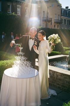 a bride and groom standing next to a table with wine glasses on it in front of a fountain