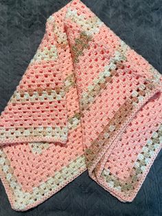 two crocheted pink and white squares on a black surface with one folded up