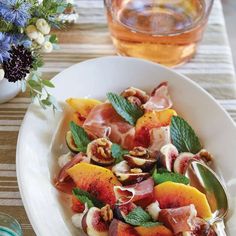 a white bowl filled with fruit and nuts on top of a table next to a glass of water