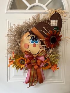 a scarecrow door hanger decorated with sunflowers and an orange pumpkin hat