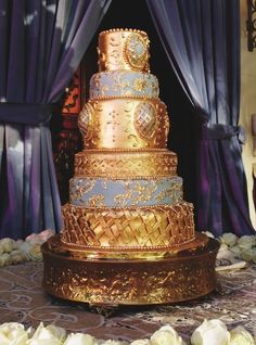 a large multi layer cake sitting on top of a table next to blue drapes