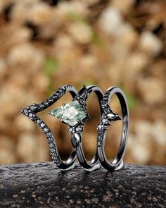 two wedding rings sitting on top of a rock next to another ring with an emerald stone in the middle