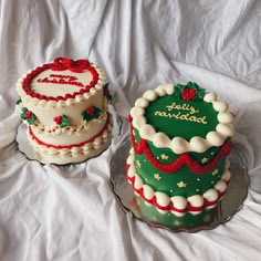 two decorated cakes sitting on top of a white cloth covered tablecloth, one is green and the other is red