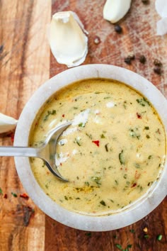 a white bowl filled with soup sitting on top of a wooden table next to garlic and cloves